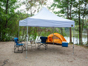 A Compact Shelter canopy set up at a lakeside campsite with camping chairs, a table, and a tent in the background, providing shade and outdoor comfort.